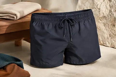 Short de bain boxer bleu-noir avec cordon de serrage, posé en studio sur un fond minéral clair.